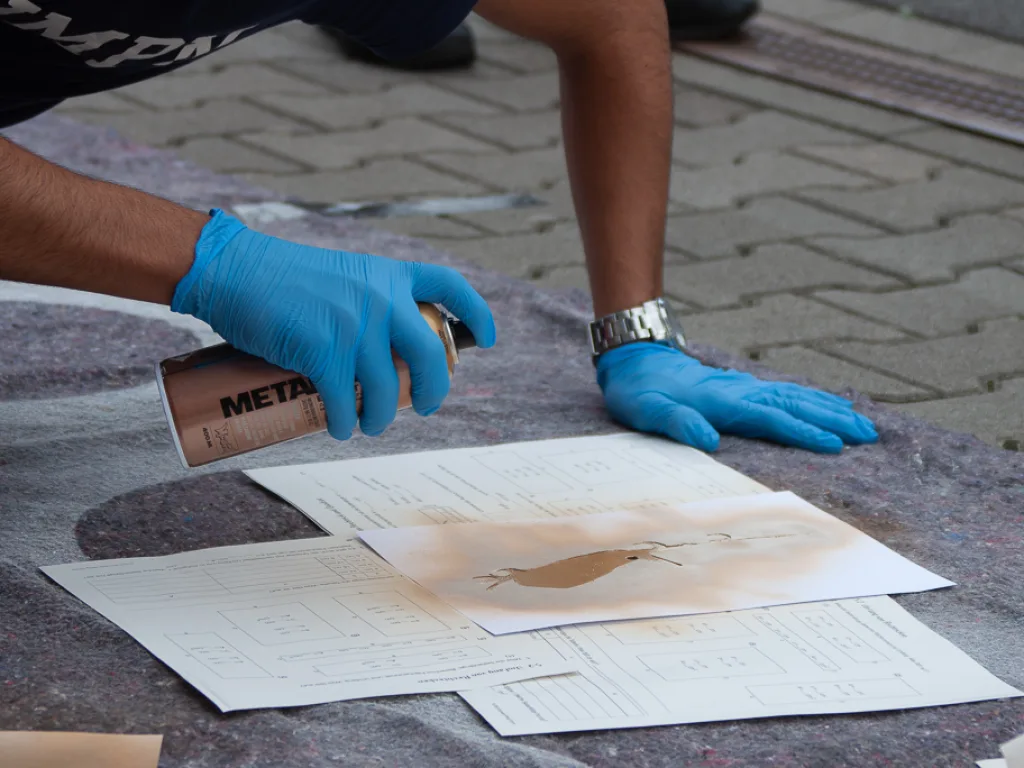 Hände in Schutzhandschuhen bearbeiten ein Blatt.